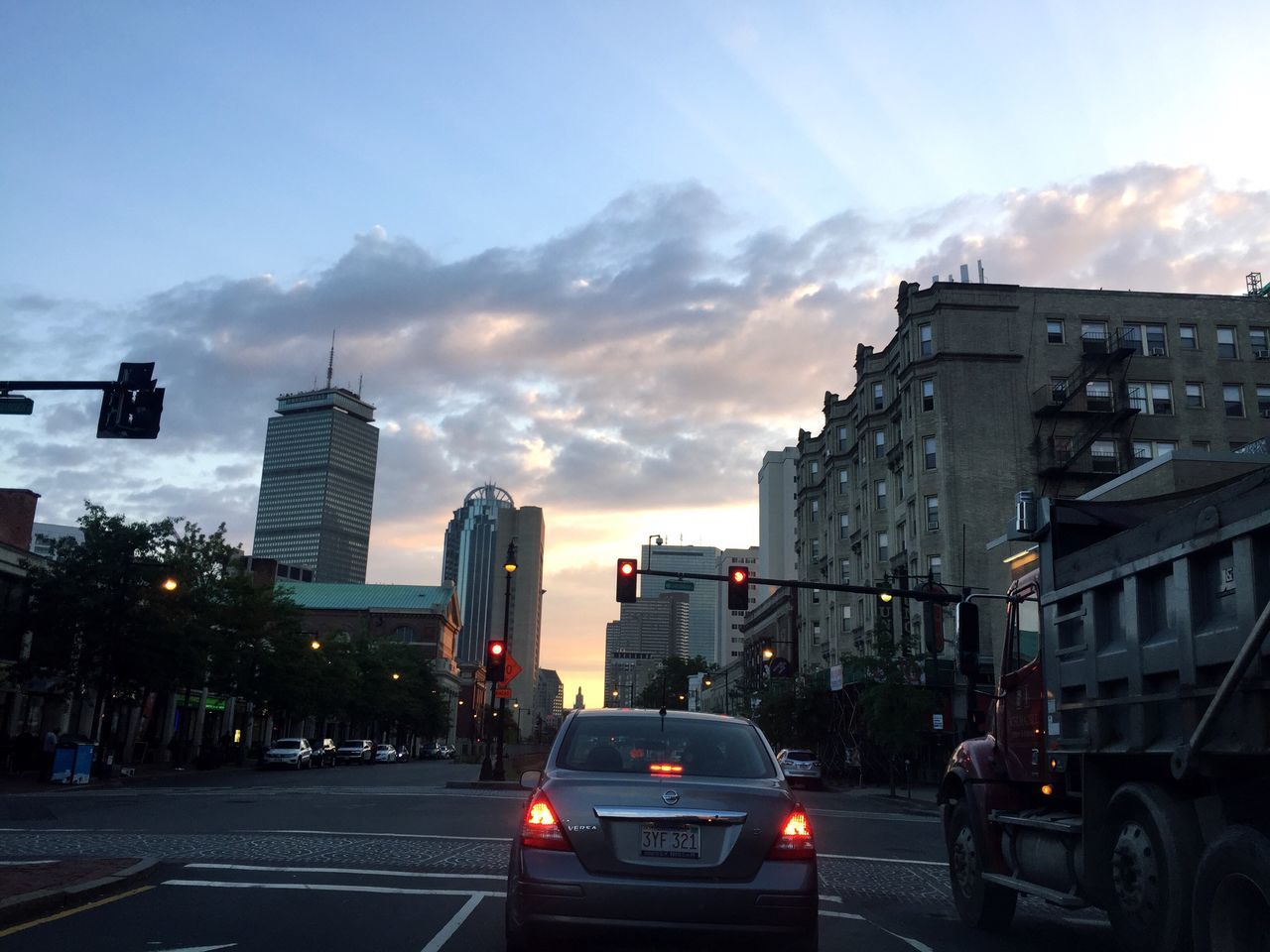 car, transportation, land vehicle, built structure, architecture, mode of transport, building exterior, sunset, street, city, road, sky, cloud, cloud - sky, skyscraper, outdoors, travel destinations, city life, vehicle, growth, urban skyline, moody sky, tail light, office building, rush hour