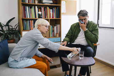 Female psychotherapist pouring water in glass while male patient wiping his face with handkerchief at office