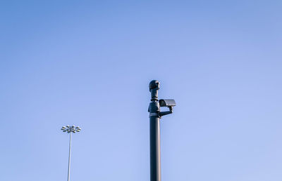 Low angle view of surveillance camera against clear blue sky