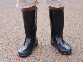 Low section of woman wearing rubber boot standing on road