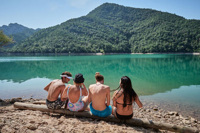 Rear view of women sitting on lake against mountains