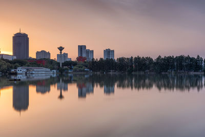 Scenic view of lake by buildings against sky during sunset