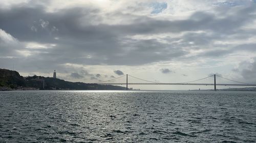 Suspension bridge over sea against cloudy sky