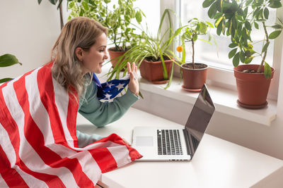 Happy woman employee sitting wrapped in usa flag, shouting for joy in office workplace, celebrating