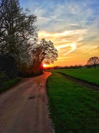 Empty road amidst field against sky during sunset