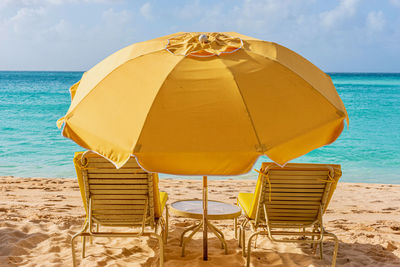 Deck chairs on beach by sea against sky