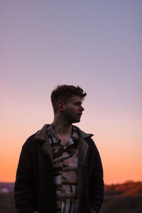 Young man looking away against sky during sunset
