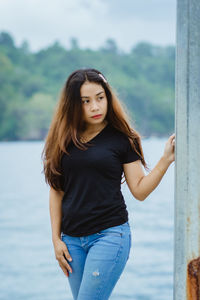 Portrait of young woman standing against sea and forest blur background