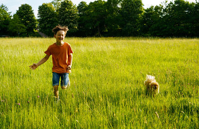 A boy runs through a summer field with small pomeranian dog