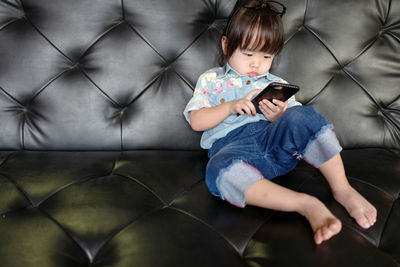 Full length of cute girl using mobile phone while sitting on sofa