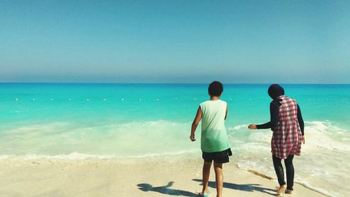 Rear view of men standing on beach against sky