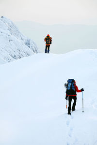 Low angle view of mountaineers climbing snowcapped mountain against sky