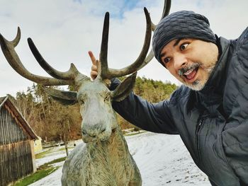 Smiling man by reindeer statue during winter