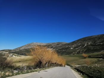 Road by mountain against clear blue sky