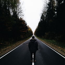 Rear view of man standing on country road amidst trees against clear sky