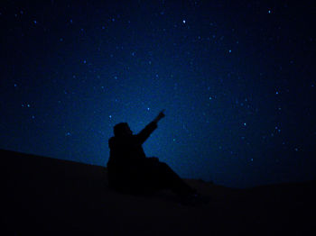 Silhouette person sitting on rock against sky at night