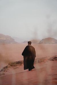 Rear view of man walking at desert against sky