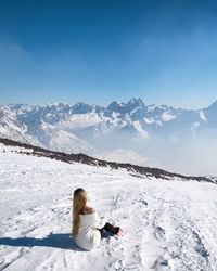 Woman sitting on snowcapped mountain against sky