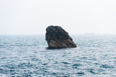 Rock formation in sea against clear sky