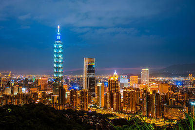 Illuminated modern buildings in city against sky at night