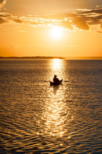 Silhouette man in sea against sky during sunset