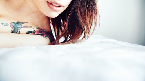Cropped image of shirtless woman with tattoo on shoulder lying in bed