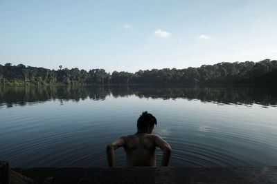 Rear view of shirtless man standing in lake against sky