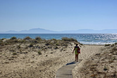 Rear view of woman walking on beach against clear sky