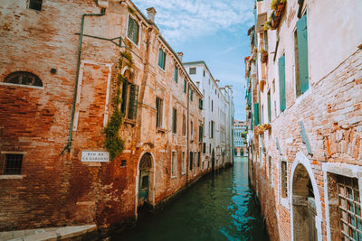 Canal amidst old buildings in city against sky