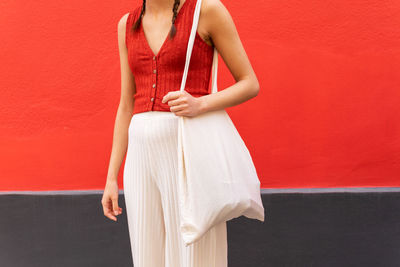 Crop view of anonymous trendy female with eco friendly textile bag standing on street near red building in city