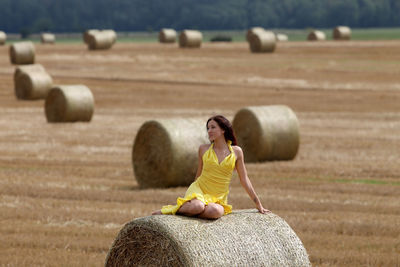 Woman sitting on hay bale at agricultural field