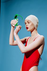 Side view of young woman drinking water against blue sky