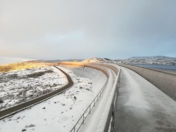 Road by snow covered landscape against sky