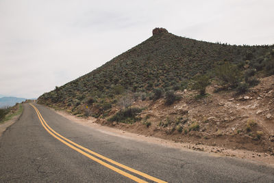 Empty country road passing through arid landscape against sky