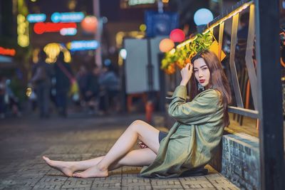 Young woman sitting in city at night