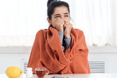 Sick woman wearing blanket sitting at home