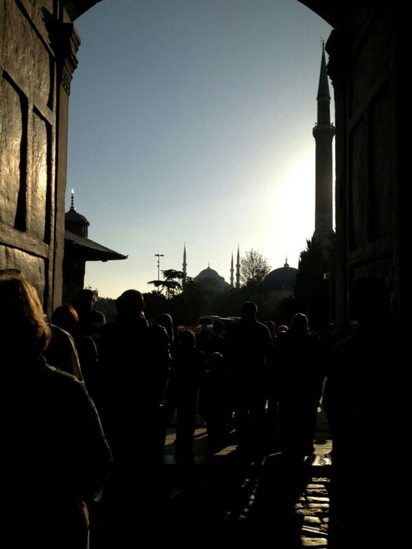 clear sky, built structure, architecture, men, building exterior, large group of people, person, silhouette, lifestyles, sunlight, leisure activity, sky, copy space, sun, medium group of people, sunset, city, sunbeam, indoors