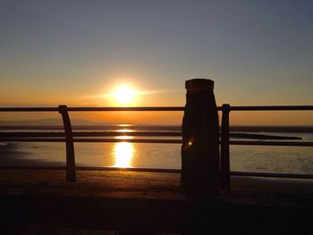 Silhouette wooden post on beach against clear sky during sunset