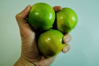 Close-up of hand holding apple against white background