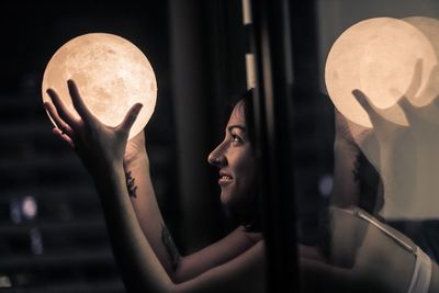 Side view of woman holding glass window at night
