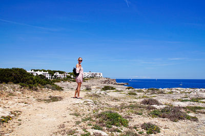 Portrait of woman standing footpath leading towards sea against blue sky