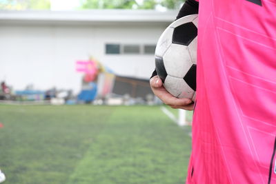 Midsection of man holding playing soccer ball while standing on field