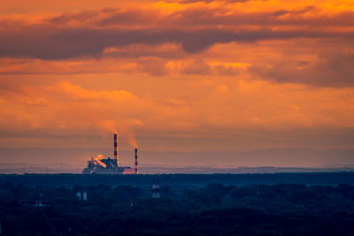 Silhouette factory against sky during sunset