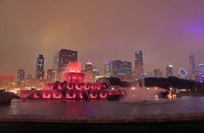 Illuminated modern buildings in city against sky at night