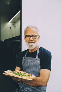 Confident senior owner with food plate standing against commercial land vehicle