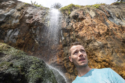 Portrait of young man standing against waterfall