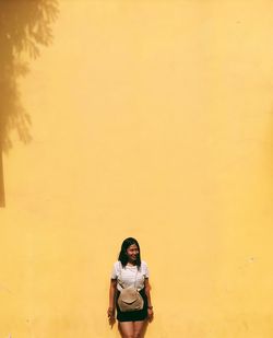 Woman looking away while standing against yellow wall