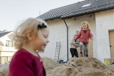 Girl playing on heap of cement with parents at construction site