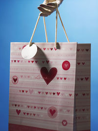 Cropped hand holding shopping bag against blue background