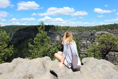 Rear view of woman looking at landscape on cliff against sky during sunny day